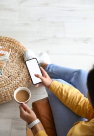 a woman sitting on the floor holding a cup of coffee and a cell phone at Spring Creek Apartments, Crestview, FL