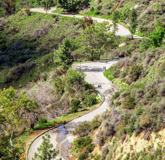 A winding road with a hill on the side and the Hollywood sign in the background.