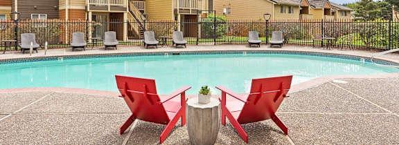 A pool surrounded by red chairs and a concrete floor.
