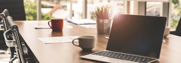 A laptop is open on a table with a cup and a pen holder.