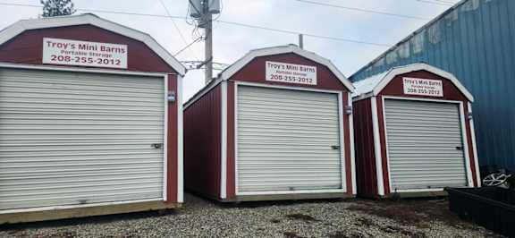 Three mini barns with red and white colors and the name Troy's Mini Barns on them.