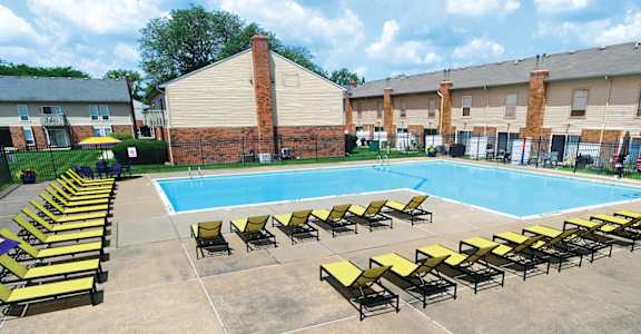 A pool surrounded by sun loungers and a brick building.