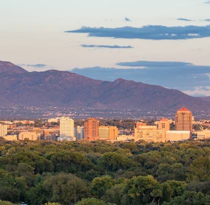 A cityscape with buildings and trees in the foreground and mountains in the background.