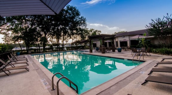 a swimming pool with lounge chairs and umbrellas in front of a building