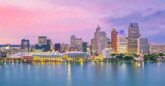A city skyline at dusk with buildings reflecting in the water.