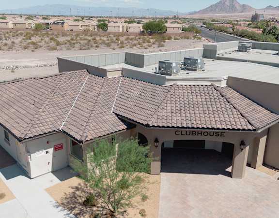 A clubhouse with a brown roof is surrounded by a parking lot and other buildings.