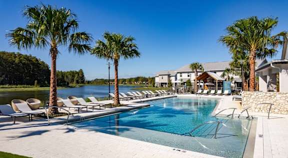 A pool surrounded by palm trees and lounge chairs.
