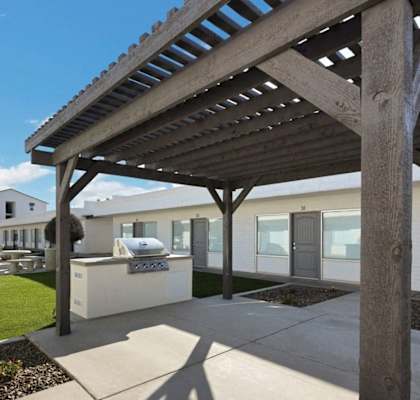 A wooden pergola is in front of a building with a white exterior.