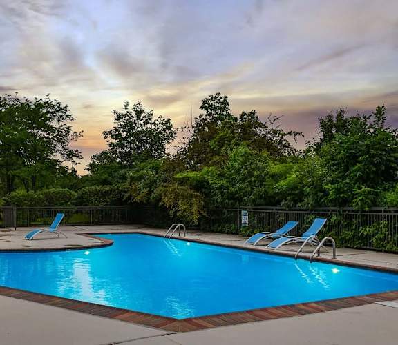 A swimming pool in front of a house with a sunset in the background.