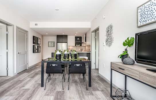 Staged dining room and kitchen, with dark modern furniture.