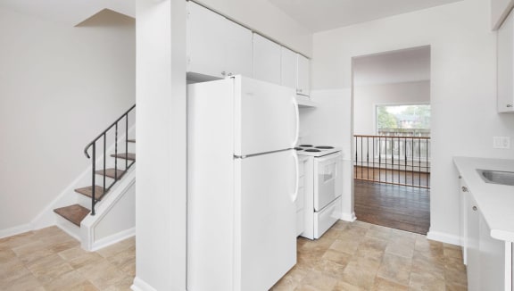 Kitchen with white appliances and cabinets. Living room and dining room seen from the kitchen as well as stairs to go upstairs.