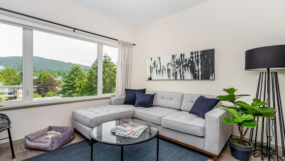 Furnished living room, with expansive window showcasing the beautiful greenery beyond.