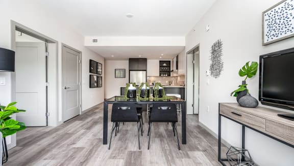 Staged dining room and kitchen, with dark modern furniture.