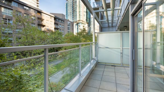 View of a large balcony, overlooking lush green trees on a quiet, clean street.