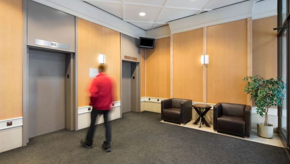 Lobby with 2 chairs, elevators and person waiting for the elevator