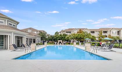 A large swimming pool surrounded by lounge chairs and umbrellas in a residential area.