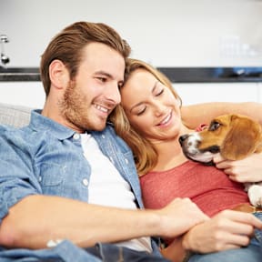 A man and woman are sitting on a couch with a dog between them.