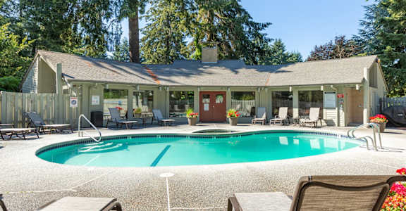 A pool in front of the clubhouse with a pool deck and chairs.