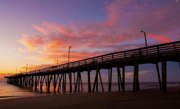 A long pier extends into the water at sunset.