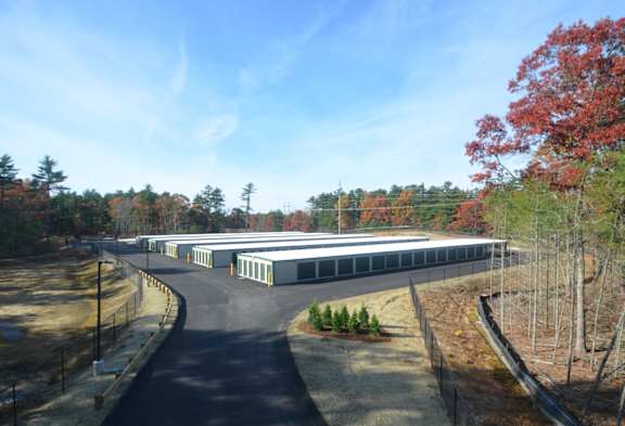 A long building with a grey roof is surrounded by trees.