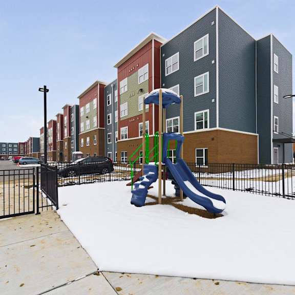 A playground with a slide and a fence in front of apartment buildings.