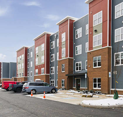 A row of apartment buildings with cars parked in front.