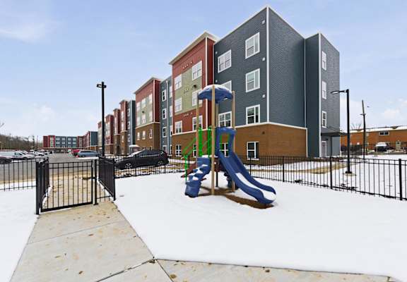A playground with a slide and a fence in front of apartment buildings.