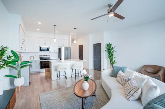A modern living room with a white sofa and a kitchen in the background.