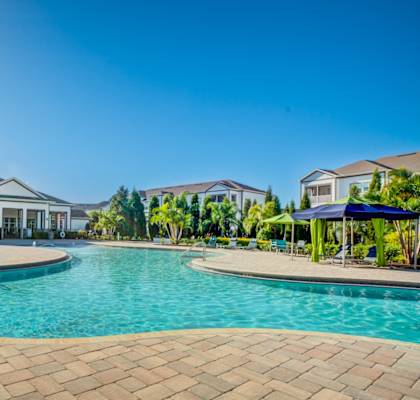 A large swimming pool surrounded by a brick patio and a house with a white exterior.at Century Ariva, Lakeland, Florida