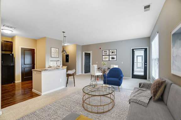 a living room with a couch a chair a table and a kitchen in the background