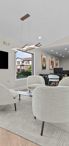 A modern living room with a large window, a flat screen TV, and a set of white chairs at Park On Canal Apartments - Clinton Twp, MI Apartments, Michigan