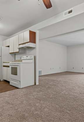 an empty living room with a kitchen and a ceiling fan