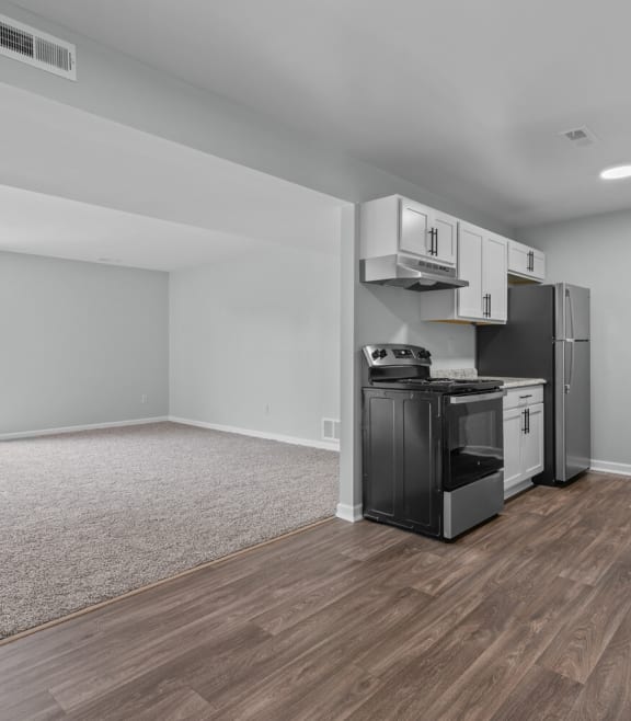 an empty living room with a kitchen with a stove and refrigerator
