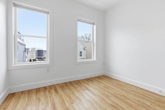 A room with wooden flooring and two windows.