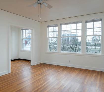 A room with a ceiling fan and two windows.