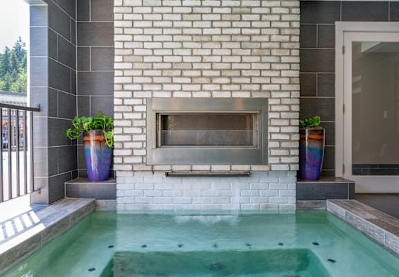 A small pool with a fireplace in the middle of a white brick wall.