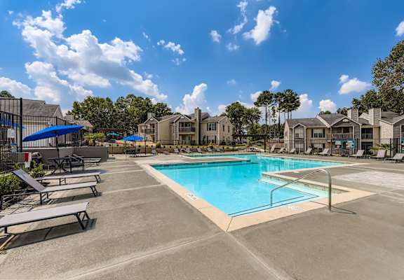 A swimming pool surrounded by sun loungers and apartment buildings.