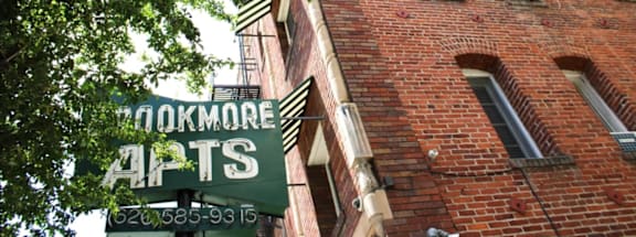 A brick building with a green sign that says "Cookmore Apts" on it.