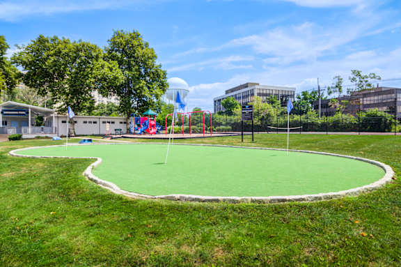A green artificial turf in the foreground with a playground and buildings in the background at Premier at Cherry Hill, New Jersey 08002