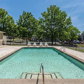 A swimming pool surrounded by trees and a building in the background.