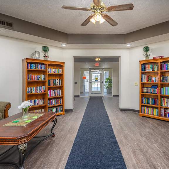 A room with a ceiling fan and bookshelves filled with books.