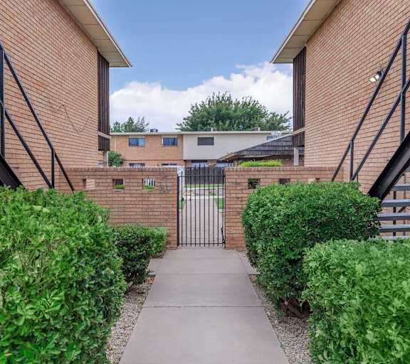 A brick building with a gate in the middle of a green hedge.