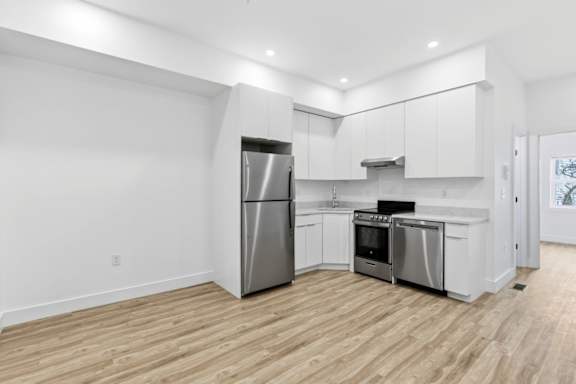 A modern kitchen with stainless steel appliances and wooden flooring.