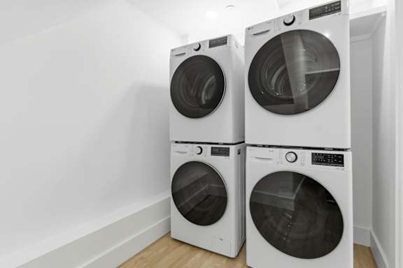 Three white front load washing machines in a laundry room.