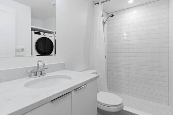 A white bathroom with a toilet, sink, and a washing machine in the corner.