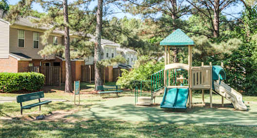 A playground with a green slide and a wooden swing set.