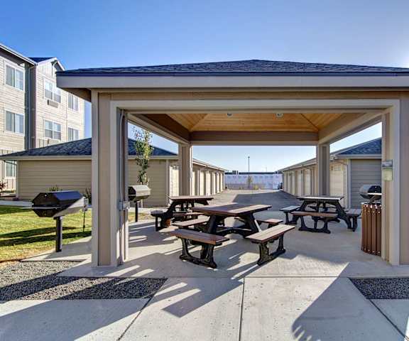 The covered outdoor grilling area with park tables, grills, and the rentable garages in the background at Prairie Vista Apartment Homes. 