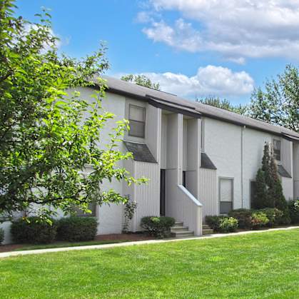 a white apartment building with a green lawn and trees