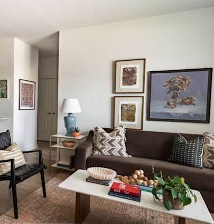 A living room with a brown couch, a white table, and a kitchen area in the background.