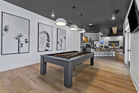 A pool table is in the middle of a room with wood flooring and three framed pictures on the wall. at Litchford 315 Apartments, Raleigh, NC, 27615
